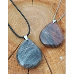 Deux pendentifs goutte en pierre de lune noire polie, l’un sur cordon noir et l’autre sur chaîne argentée, posés sur une tranche de bois, bijoux en pierre naturelle associés à la douceur émotionnelle, à l’ancrage et à l’harmonie intérieure.