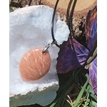 Pendentif rond en pierre de soleil sur cordon noir, posé près de cristaux blancs et décor violet, bijou en pierre naturelle lié à la bonne humeur, au dynamisme et à l’équilibre intérieur