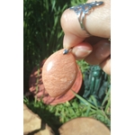 Pendentif goutte en pierre de soleil tenu en main sur feuilles vertes, pierre naturelle associée à la spontanéité, au courage paisible et à la chaleur du cœur.