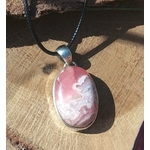 Pendentif rhodochrosite ovale rose marbré en argent 925 sur cordon noir, posé sur bois en lumière naturelle, bijou en pierre naturelle évoquant le calme affectif, la bienveillance et l’harmonie intérieure.
