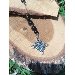 Bijou de rétroviseur « nœud de sorcière » : perles de tourmaline noire sur cordon, pendentif nœud celtique argenté, suspendu devant une tranche de bois et feuillage vert. Création Magic Gaïa, pour protection, ancrage et apaisement.