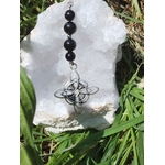 Bijou de rétroviseur « nœud de sorcière » : perles noires sur cordon, pendentif nœud celtique argenté, posé sur un amas de quartz blanc au milieu de feuillages verts. Création Magic Gaïa, pour protection, ancrage et apaisement.