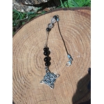 Bijou de rétroviseur « nœud de sorcière » : perles de tourmaline noire et petites perles claires sur cordon, pendentif nœud celtique argenté, posé sur rondin de bois avec feuillage vert. Création Magic Gaïa, pour protection, ancrage et apaisement.