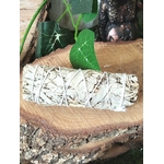 Bâton de sauge blanche à brûler (fumigation/smudge) ficelé, posé sur rondin de bois, feuilles vertes et décor ésotérique. Pour rituel, méditation, purification énergétique, nettoyage des lieux, protection, clarté, apaisement.