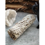 Bâton de sauge blanche à brûler (fumigation/smudge) ficelé, posé sur surface grise avec amas de quartz blanc. Accessoire ésotérique pour rituel, méditation, purification énergétique, nettoyage des lieux, protection, clarté et apaisement.