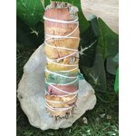 Bâton de sauge 7 chakras à brûler (fumigation/smudge), décoré de pétales de rose multicolores, ficelé, présenté debout sur amas de quartz blanc et feuillage vert. Pour rituel, méditation, purification énergétique, protection, clarté et apaisement.