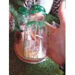 Spell jar abondance Magic Gaïa, flacon en verre scellé cire verte, riz et cannelle, tenu en main sur décor mousse