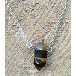 Pendentif pointe œil de tigre sur chaîne en acier inoxydable, photo sur fond bois clair texturé, pierre naturelle associée à la lucidité, à l’aplomb et à la présence à soi.