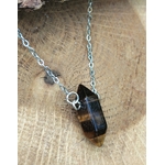 Pendentif pointe œil de tigre sur chaîne en acier inoxydable, posé sur fond bois brut, bijou en pierre naturelle évoquant la force calme, la volonté et l’équilibre émotionnel.