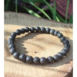 Bracelet Pierre de Lave 6 mm sur élastique, perles noires poreuses sur tranche de bois avec herbes, ancrage et force intérieure.