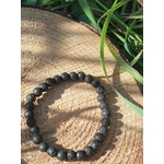 Bracelet Pierre de Lave 6 mm sur tranche de bois avec herbes et ombres douces, énergie stable, force calme et ancrage.