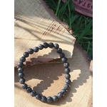 Bracelet en pierre volcanique 6 mm sur fond bois et herbes, perles de basalte noires, persévérance, stabilité et apaisement mental.