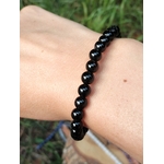 Bracelet Onyx noir en perles rondes brillantes porté au poignet en extérieur, retenue, assurance et limites émotionnelles.