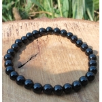 Bracelet Onyx noir en perles rondes sur élastique, posé sur tranche de bois avec herbes vertes, aplomb, constance et sang-froid.