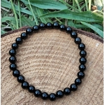 Bracelet Onyx noir 6 mm en perles rondes sur élastique, décor bois et herbes vertes floues, endurance, volonté et clarté mentale.
