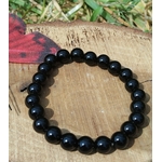 Bracelet Onyx noir 8 mm en perles noires lisses sur bois naturel et fond végétal, assurance, persévérance et lucidité.