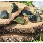 Pierres roulées de serpentine vert olive, posées sur une tranche de bois clair en décor naturel, lumière douce et chaleureuse; pierre associée à l’apaisement, à l’ancrage et à l’équilibre émotionnel.