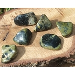 Pierres roulées de serpentine vert olive, posées sur une tranche de bois clair en décor naturel, lumière douce et chaleureuse; pierre associée à l’apaisement, à l’ancrage et à l’équilibre émotionnel.
