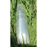 Tour en sélénite blanche polie posée dans l’herbe, prise de vue rapprochée, lumière naturelle, pour une énergie légère et atmosphère zen.