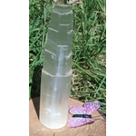 Tour en sélénite translucide photographiée en extérieur sur fond d’herbe, avec un papillon violet au bas de l’image, ambiance douce et apaisante.