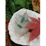 Création Magic Gaïa : boucles d’oreilles en aventurine verte sur crochets dorés, posées sur amas de quartz blanc avec feuille rouge, fond végétal, pour apaisement et harmonie.