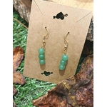 Boucles d’oreilles création Magic Gaïa en aventurine verte, posées sur amas blanc avec feuille rouge, fond végétal, pour une ambiance harmonieuse et sereine.