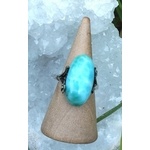 Bague réglable en argent avec cabochon de larimar bleu, posée sur un présentoir conique devant des cristaux givrés, pour apaiser, clarifier et inviter la douceur.
