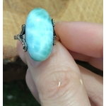 Bague larimar réglable en argent, tenue entre deux doigts devant un fond en bois doré, pour apaiser et encourager une expression sereine.
