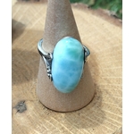 Bague larimar en argent réglable sur support conique, posée sur bois naturel avec touche de verdure, pour douceur et calme intérieur.