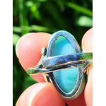 Vue arrière de la bague larimar en argent réglable, tenue entre les doigts avec une tige dherbe, fond vert flou, pour apaiser et exprimer sa vérité.