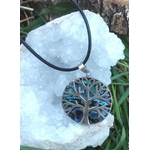 Pendentif arbre de vie en abalone et argent 925 sur cordon noir, posé sur amas clair de quartz près d’herbe et d’écorce, bijou en nacre naturelle lié à l’équilibre intérieur, au calme du cœur et au recentrage.