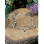 Chaîne de cheville en acier inoxydable avec perles de labradorite et breloques triquetra, posée sur rondin de bois près d’un papillon décoratif, idéale pour l’ancrage et la protection au quotidien.