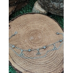 Chaîne de cheville en acier inoxydable avec perles de labradorite et breloques triquetra, posée sur un rondin de bois aux cernes visibles, pour l’ancrage, la protection et la confiance