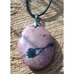 Pendentif ovale en rhodonite polie sur cordon noir, posé sur une tranche de bois au soleil, bijou en pierre naturelle évoquant le pardon, le recentrage et la paix émotionnelle.