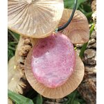 Pendentif rond en rhodonite sur cordon noir, posé sur champignons et herbes au soleil, bijou en pierre naturelle associé à la douceur, au réconfort affectif et à l’équilibre du cœur.