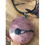 Pendentif rond en rhodonite rose sur cordon noir, posé sur une rondelle de bois, bijou en pierre naturelle évoquant le pardon, la douceur du cœur et la stabilité émotionnelle.