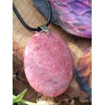 Pendentif ovale en rhodonite rose sur cordon noir, posé sur bois brut près d’une aile de papillon violette, bijou en pierre naturelle lié à la douceur intérieure, au soutien émotionnel et à la paix du cœur.