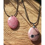Deux pendentifs en rhodonite sur cordon noir, posés sur une tranche de bois au soleil, bijoux en pierre naturelle associés à la douceur du cœur, au réconfort et à la stabilité émotionnelle.