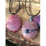 Deux pendentifs en rhodonite rose sur cordons noirs, posés sur écorce et plume violette, bijoux en pierre naturelle associés au réconfort, à l’harmonie émotionnelle et à la douceur relationnelle.