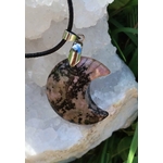 Pendentif lune en rhodonite aux nuances rose et noir, suspendu sur géode blanche avec corde et feuillage, bijou en pierre naturelle évoquant le réconfort, la tendresse et la stabilité émotionnelle.