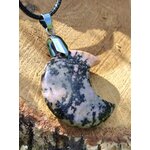 Pendentif lune en rhodonite rose veinée de noir sur cordon, posé sur une tranche de bois avec feuillage en arrière-plan, bijou en pierre naturelle lié à l’ancrage doux, au calme du cœur et au soutien émotionnel.