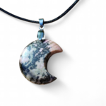 Pendentif lune en rhodonite marbrée rose et noir sur fond blanc, cordon noir et bélière argentée, bijou en pierre naturelle relié à l’apaisement, au pardon et à l’équilibre intérieur.