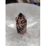 Pointe de rhodonite rose veinée de noir posée dans un bol en sélénite blanche, lumière douce, pour soutenir l’apaisement et l’équilibre émotionnel.