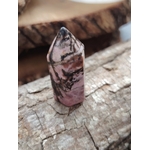 Pointe de rhodonite polie aux veines noires posée sur une écorce de bois, décor nature brun doré en lumière douce, idéale pour accompagner l’apaisement et la compassion au quotidien.