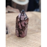 Pointe de rhodonite rose marbrée de veines noires posée debout sur une planche de bois clair, fond flou chaleureux, pour inviter à l’apaisement et à la douceur du cœur.