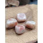 Quatre pierres roulées en pierre de soleil, posées sur une rondelle de bois, teintes crème et pêche, pour cultiver joie, confiance et vitalité.