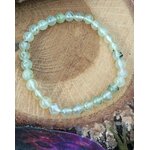 Bracelet préhnite 6 mm posé sur rondin de bois dans une ambiance douce, clarté mentale, équilibre émotionnel et respiration plus paisible