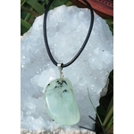 Pendentif en préhnite vert d’eau sur cordon noir, posé sur un amas de quartz scintillant parmi des brins d’herbe, bijou naturel évoquant la fraîcheur émotionnelle, le relâchement et la paix mentale.