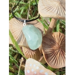 Pendentif en préhnite vert d’eau sur cordon noir, posé sur tranches de bois façon champignons au milieu d’herbes, bijou en pierre naturelle lié à la légèreté, à la respiration intérieure et à l’harmonie du cœur.