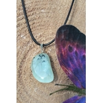 Pendentif préhnite vert d’eau sur cordon noir, posé sur tranche de bois avec papillons violets et brins d’herbe, bijou en pierre naturelle associé à la douceur, au renouveau et à l’écoute de soi.